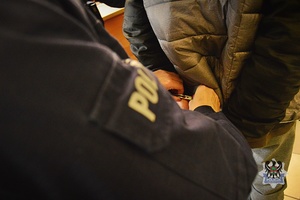 Na zdjęciu policjant zakłada kajdanki zatrzymanemu.