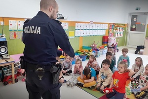 Na zdjęciu policjant prowadzi z dziećmi pogadankę o bezpieczeństwie.