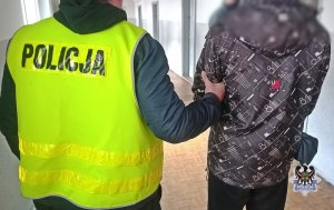 Na zdjęciu policjant prowadzi zatrzymanego mężczyznę.