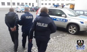 Policjanci prowadzą drugiego zatrzymanego do radiowozu