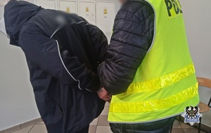 Na zdjęciu policjant zakłada zatrzymanemu kajdanki.