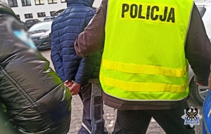 Na zdjęciu policjant prowadzi jednego z zatrzymanych mężczyzn do radiowozu.