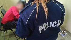 Na zdjęciu policjantka pilnuje zatrzymanego listem gończym mężczyzny.