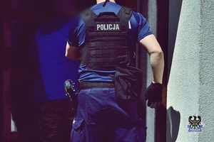 Na zdjęciu policjantka prowadzi zatrzymanego mężczyznę do budynku.