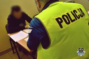 Na zdjęciu policjant prowadzi czynności procesowe z zatrzymanym mężczyzną - drugie ujęcie.