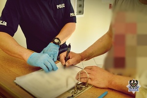Naz zdjęciu mężczyzna w obecności policjanta podpisuje dokumenty.