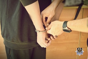 Na zdjęciu policjant zakłada kajdanki jednemu z zatrzymanych mężczyzn.