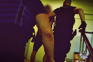 Na zdjęciu policjant prowadzi zatrzymanego mężczyznę.