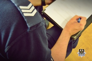 Na zdjęciu policjant pilnuje zatrzymanego mężczyzny.