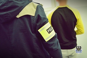Na zdjęciu policjant pilnuje zatrzymanego mężczyzny.