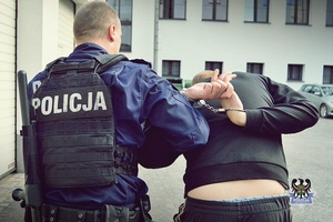 Na zdjęciu policjant prowadzi zatrzymanego mężczyznę.