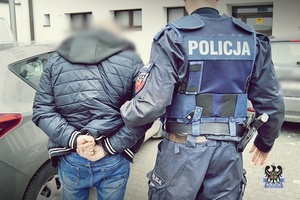 Na zdjęciu policjant prowadzi drugiego z zatrzymanych mężczyzn.