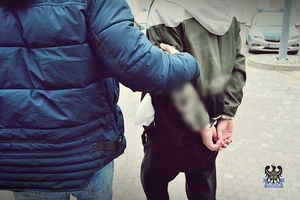 Na zdjęciu policjant prowadzi zatrzymanego  mężczyznę.