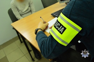 Na zdjęciu policjant wykonuje czynności procesowe z zatrzymaną kobietą.