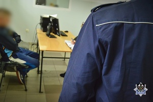 Na zdjęciu policjant pilnuje zatrzymanego mężczyzny.