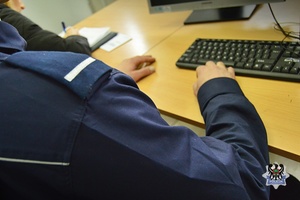 Na zdjęciu policjant pilnuje zatrzymanego mężczyzny.