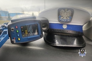 Na zdjęciu fotoradar z prędkością 104 km/h oraz czapka policyjna.