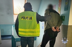 Na zdjęciu policjant prowadzi zatrzymanego mężczyznę.
