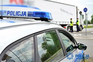 Na zdjęciu radiowóz oraz policjanci pełniący służbę na drodze.