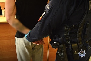 Na zdjęciu policjant zakłada kajdanki zatrzymanemu mężczyźnie.
