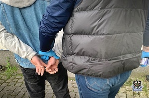 Na zdjęciu policjant prowadzi zatrzymanego mężczyznę.