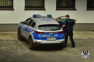 Na zdjęciu policjanci umieszczają zatrzymanego mężczyznę w radiowozie.