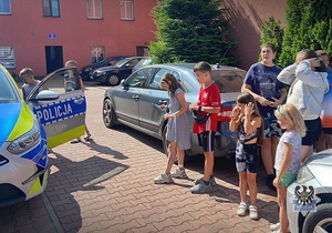 Na zdjęciu policjanci pokazują dzieciom samochód służbowy.
