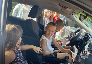 Na zdjęciu policjanci pokazują dzieciom samochód służbowy.