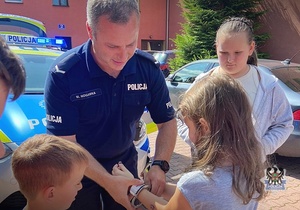 Na zdjęciu policjanci pokazują dzieciom chwyty transportowe używane przez policjantów w służbie.
