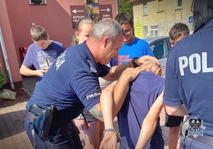 Na zdjęciu policjanci pokazują dzieciom chwyty transportowe używane przez policjantów w służbie.