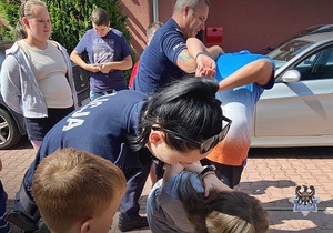 Na zdjęciu policjanci pokazują dzieciom chwyty transportowe używane przez policjantów w służbie.