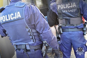 Na zdjęciu policjanci umieszczają zatrzymanego mężczyznę w radiowozie.