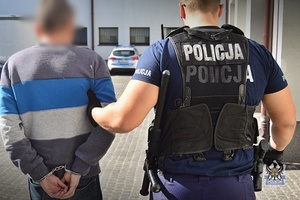 Na zdjęciu policjant prowadzi zatrzymanego mężczyznę.