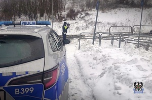 Na zdjęciu policjant oraz radiowóz w porze zimowej.
