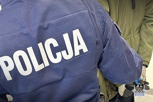 Na zdjęciu policjant pilnuje zatrzymanego  mężczyzny.