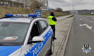 Na zdjęciu radiowóz oraz policjant z ręcznym miernikiem prędkości.