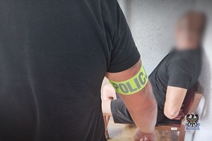 Na zdjęciu policjant pilnuje zatrzymanego mężczyzny.
