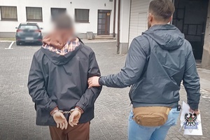 Na zdjęciu policjant prowadzi zatrzymanego mężczyznę.