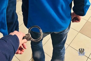 Na zdjęciu policjant zakłada kajdanki osobie poszukiwanej.