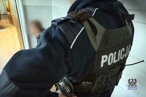 Na zdjęciu policjant pilnuje zatrzymanego mężczyzny.