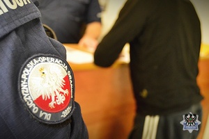 Na zdjęciu policjant pilnuje zatrzymanego mężczyzny.