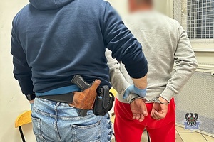 Na zdjęciu policjant pilnuje zatrzymanego mężczyzny.