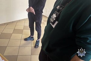 na zdjęciu policjant pilnuje zatrzymanego mężczyzny.