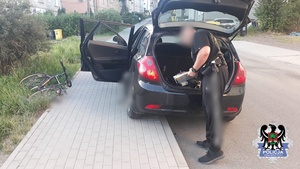policjant przy nieznakowanym radiowozie, obok  na którym poruszał się zatrzymany