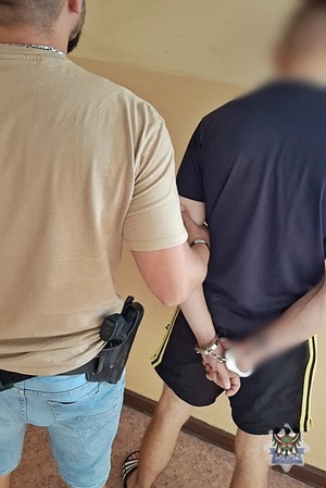 Na zdjęciu policjant pilnuje zatrzymanego mężczyzny.