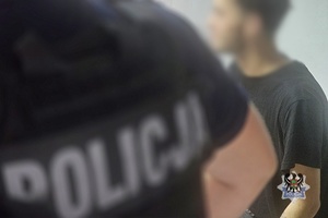 Na zdjęciu policjant pilnuje zatrzymanego mężczyzny.