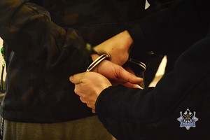Na zdjęciu policjant zakłada kajdanki zatrzymanemu.