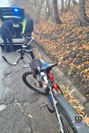 Na zdjęciu policjant bada kontrolowanego rowerzystę przy radiowozie oraz kontrolowany rower.