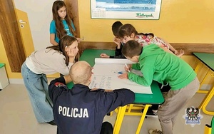 Na zdjęciu policjant oraz uczniowie szkoły podstawowej podczas zajęć.