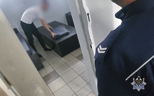 Na zdjęciu policjant sprawdza celę z zatrzymanym mężczyzną.